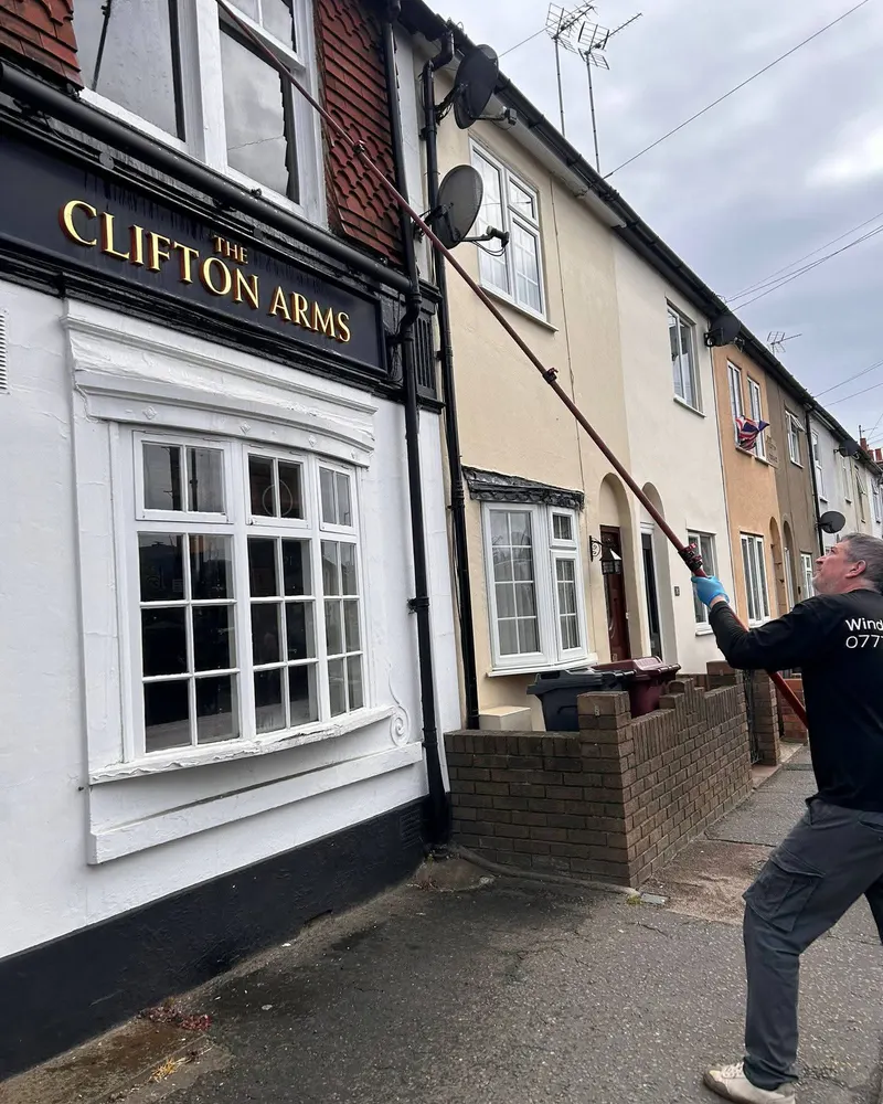 Stephen cleaning the windows above a pub front with a water-fed pole