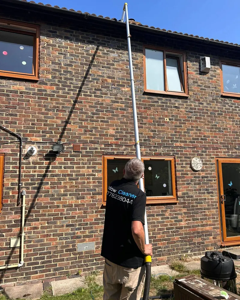 Stephen cleaning the upstairs windows of a brick house with a water-fed pole