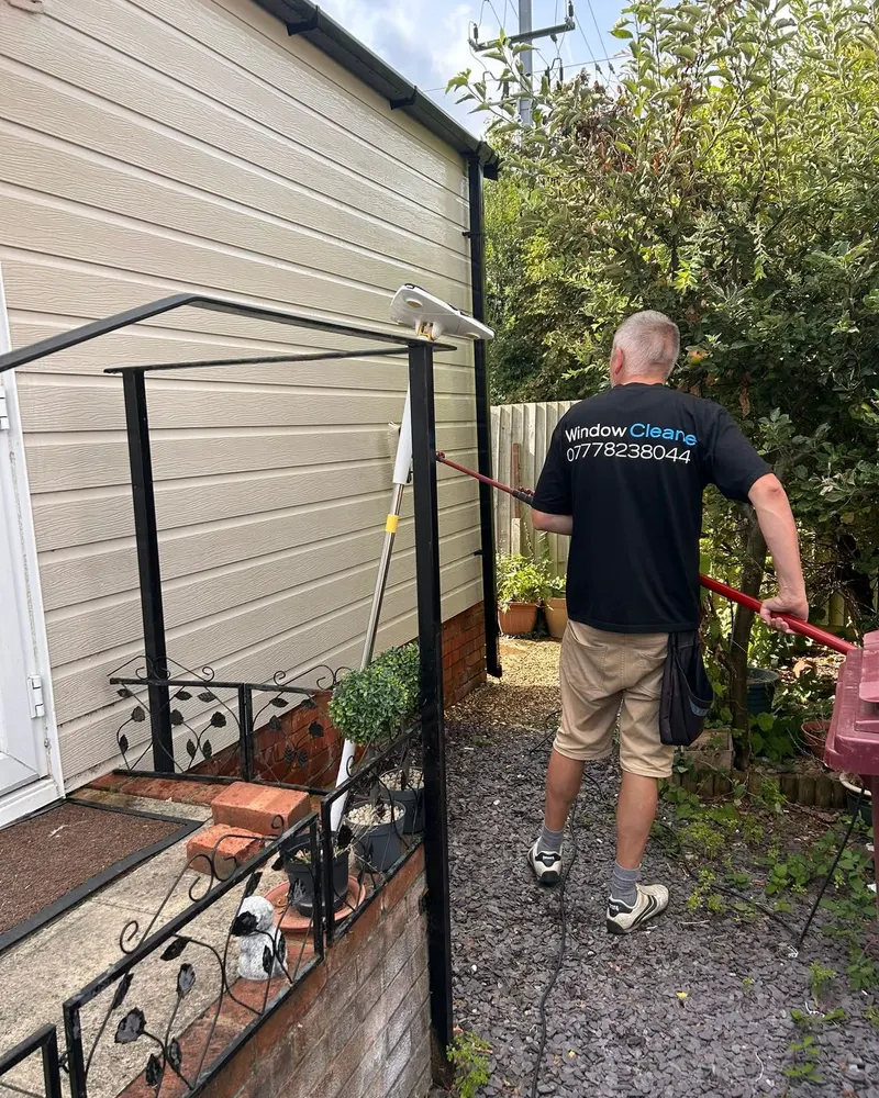 Stephen cleaning cladding at the back of a house with a pole